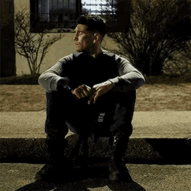 a man is sitting on the side of a street at night .