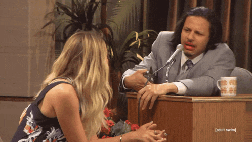 a man in a suit sits at a podium talking to a woman with the words adult swim written on the bottom