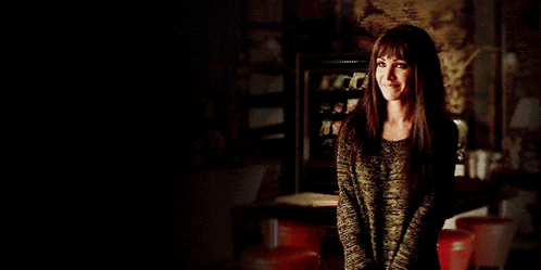 a woman in a green sweater stands in a dark room smiling