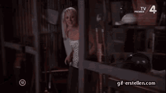 a woman in a white dress is opening a box in a warehouse with tv premier on the bottom right