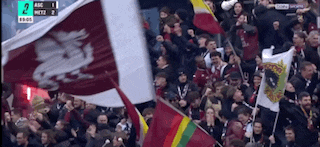 a crowd of people holding flags in a stadium with the score 2 to 1