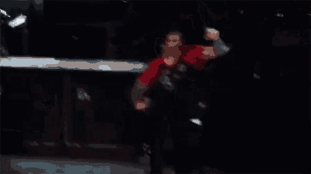 a man in a red shirt is dancing on a stage with his hands in the air .