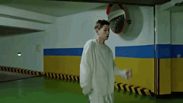 a man in a white sweater is standing in a parking garage with a mirror on the wall .