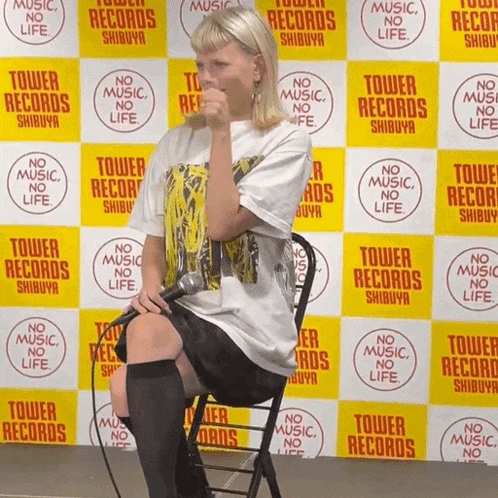 a woman is sitting in front of a tower records backdrop