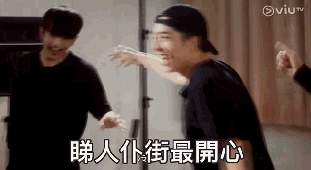 a man in a baseball cap is laughing while standing next to another man in a black shirt .