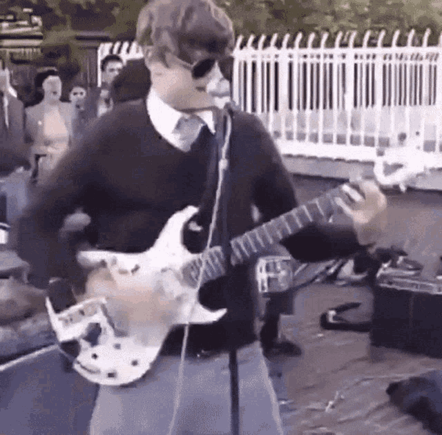 a man wearing sunglasses is playing a guitar in front of a microphone