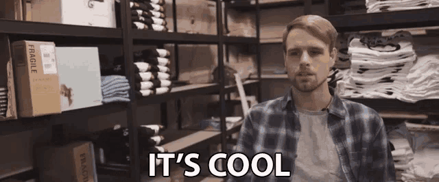 a man in a plaid shirt says it 's cool in front of a stack of fragile boxes