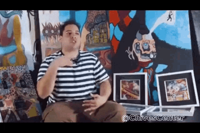 a man in a striped shirt is sitting in front of a painting of a devil
