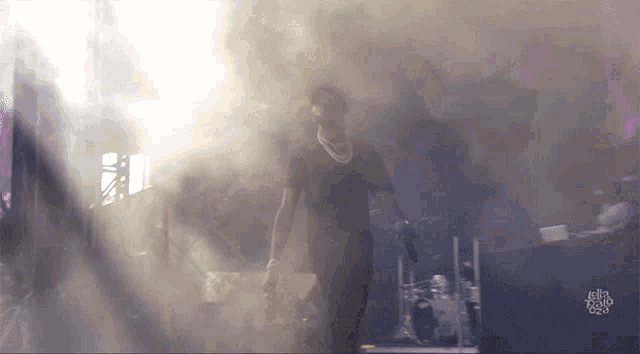 a man in a black shirt stands in front of a stage with smoke coming out of it and the word ella on the bottom