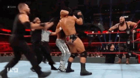 a group of wrestlers are fighting in a ring while a referee watches .