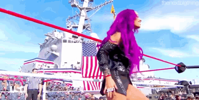 a woman with purple hair is standing in a ring with an american flag in the background .