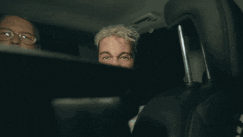 a man with blonde hair is making a funny face in the back of a car