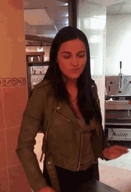 a woman in a green leather jacket stands in front of a kitchen