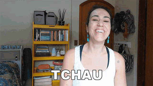 a woman is smiling in front of a yellow bookshelf and the word tchau is on the front of her shirt