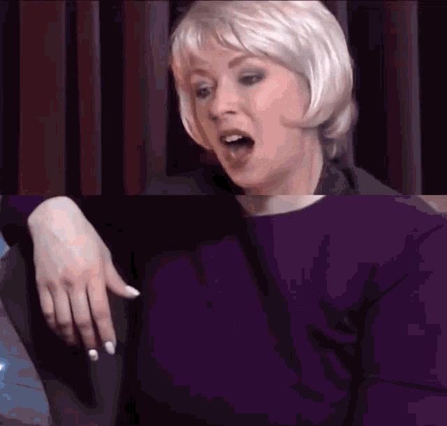 a woman wearing a purple shirt and white nails is making a surprised face