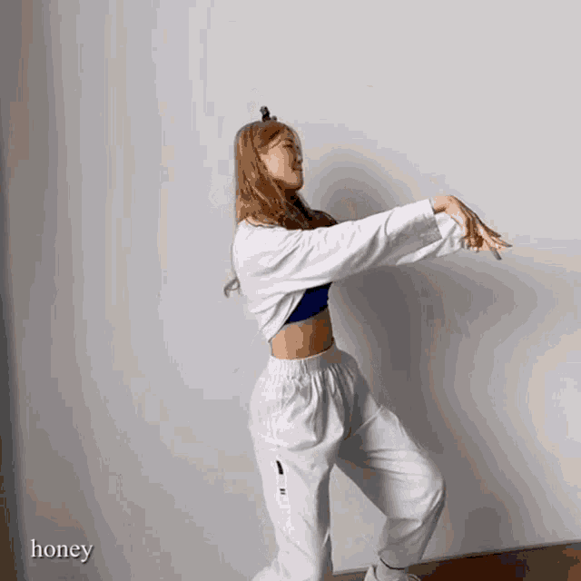 a woman in a blue top and white pants is dancing with the word honey behind her