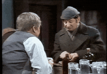 two men are sitting at a table with a bottle of alcohol