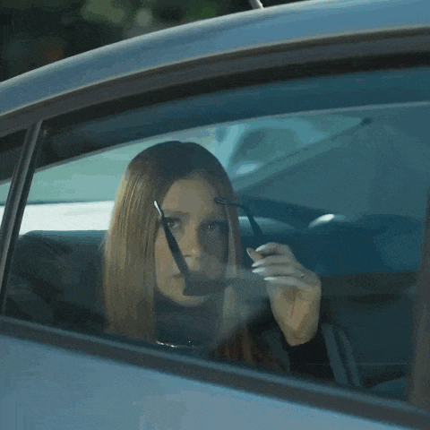 a woman in a car wearing sunglasses looks out the window