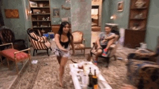 a woman in shorts is standing next to a table with a bottle of wine on it .