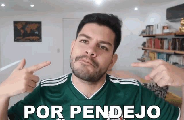 a man with a beard and mustache is pointing at himself in a green shirt that says por pendejo