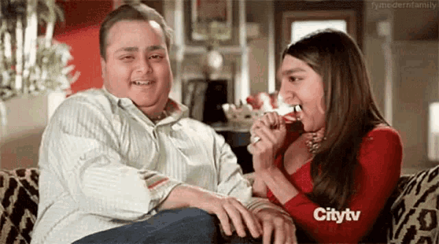 a man and a woman are sitting on a couch and the woman is eating from the man 's hand .