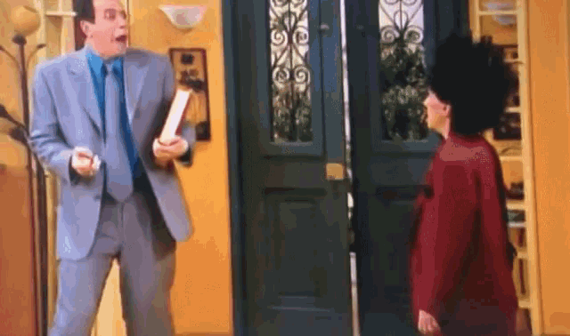 a man in a suit holds a piece of paper in front of a woman in a red sweater