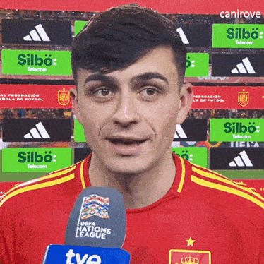 a man wearing a red shirt with yellow stripes is holding a microphone that says uefa nations league