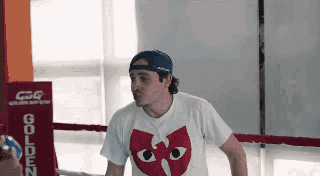 a man wearing a white shirt with a red heart on it stands in front of a sign that says golden baby gym