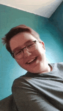 a young man wearing glasses and a grey shirt is smiling for the camera