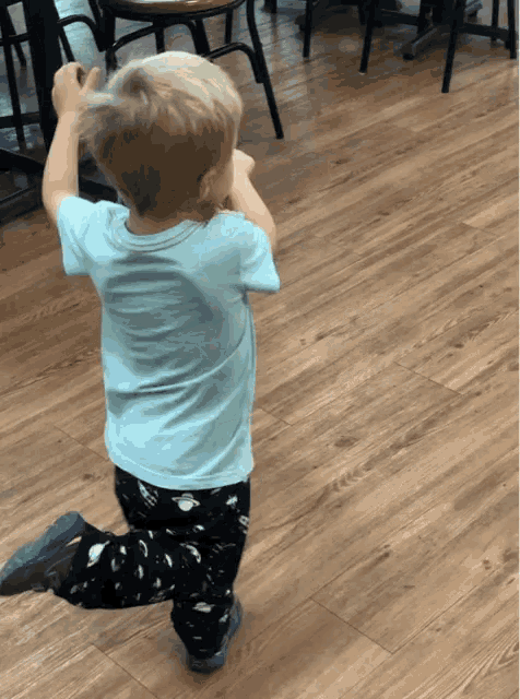 a little boy in a blue shirt and black pants is walking on a wood floor
