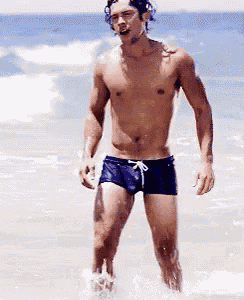a shirtless man in blue swim trunks is standing in the water