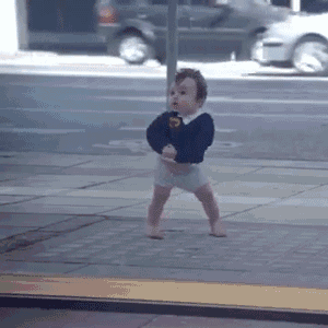 a baby is walking barefoot on a sidewalk in front of a street .