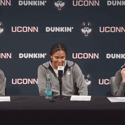 a woman stands in front of a uconn dunk sign