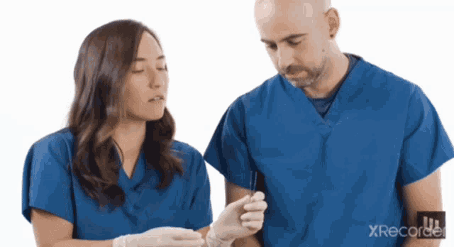 a man and a woman in blue scrubs are looking at something with xrecord in the corner