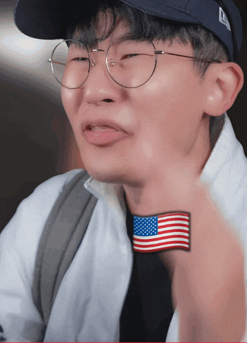 a man wearing glasses and a hat has a small american flag on his neck
