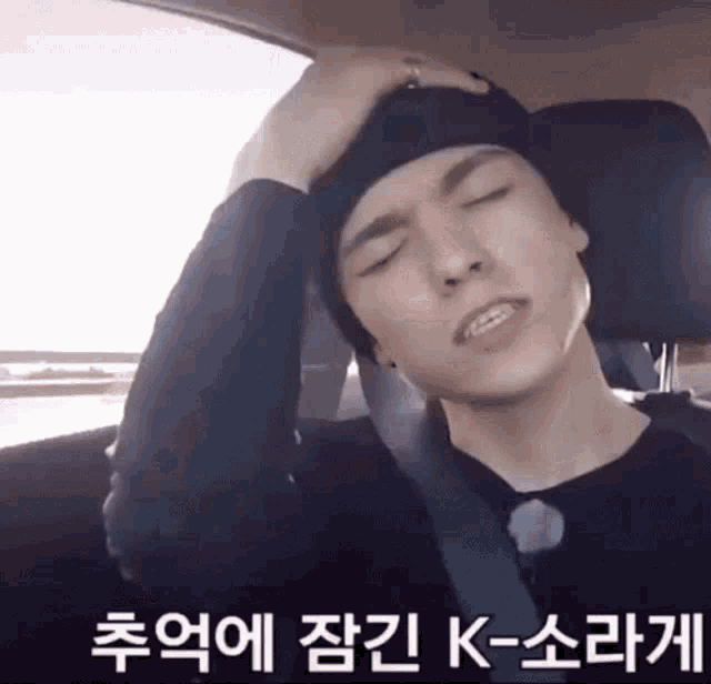a man wearing a black hat is sitting in a car with his eyes closed and his hand on his head .