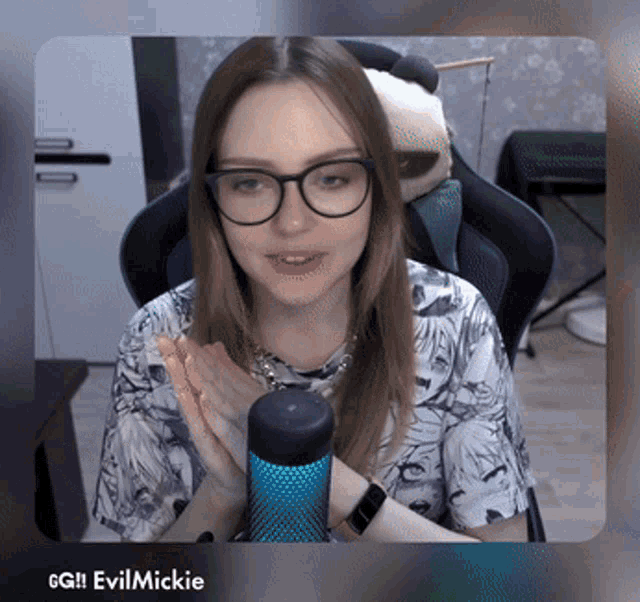 a woman wearing glasses is sitting in front of a microphone and the name evilmickie is on the bottom right