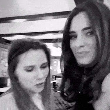 a black and white photo of two women talking to each other in a room .