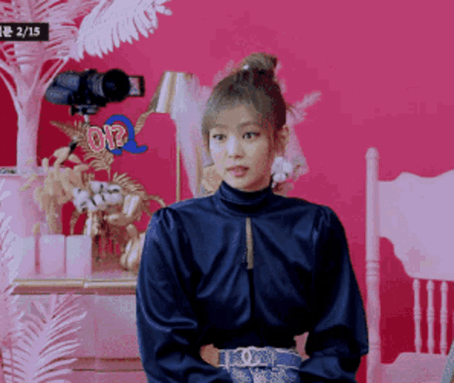 a woman in a blue shirt is sitting in front of a pink wall with a sign that says pop