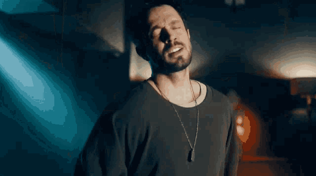 a man with a beard is wearing a necklace and singing into the camera .