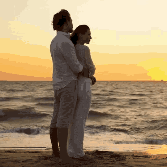 a man and woman standing on a beach looking at the ocean
