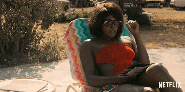 a woman is sitting in a chair reading a magazine with netflix written on the bottom