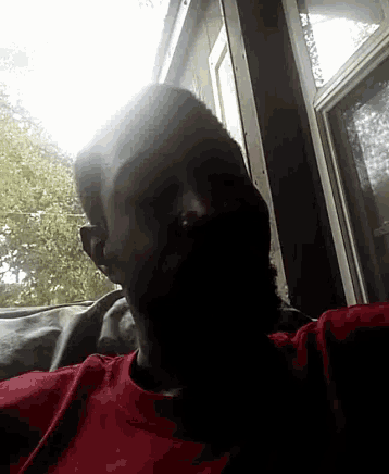 a man in a red shirt is taking a picture of himself in front of a window