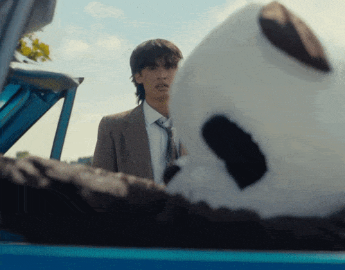 a man in a suit and tie stands next to a stuffed panda