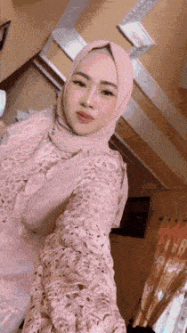a woman wearing a pink hijab and a lace dress is taking a selfie .