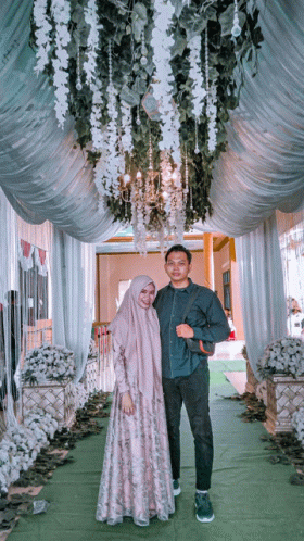 a man and a woman are posing for a picture in front of a chandelier hanging from the ceiling