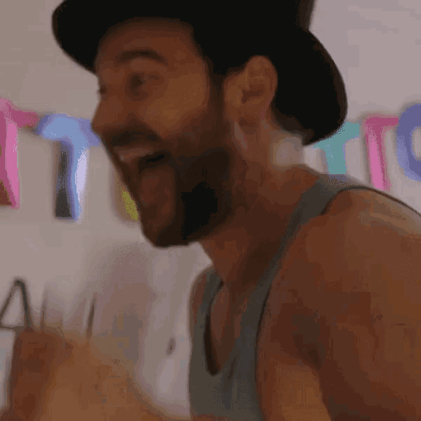 a man with a beard wearing a top hat and a tank top is laughing