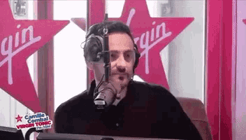 a man is talking into a microphone in front of a sign that says virgin