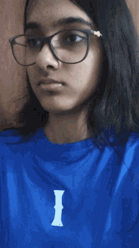 a girl wearing glasses and a blue shirt has the letter i on her chest