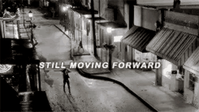 a black and white photo of a city street at night with the words `` still moving forward '' written on it .